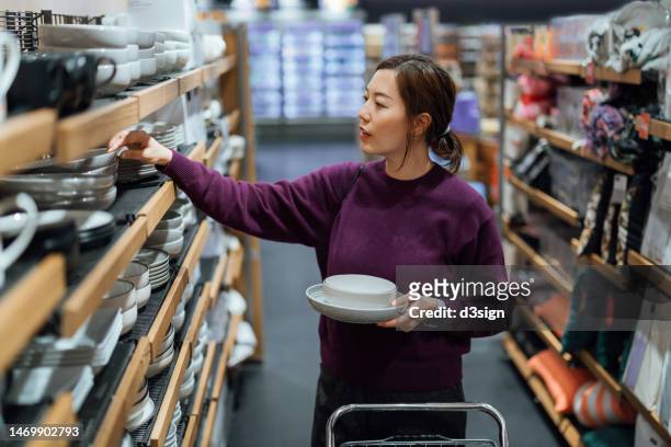 young asian woman shopping for crockery products in a homeware store. choosing new plates and bowls for home. home shopping - kitchenware shop 個照片及圖片檔