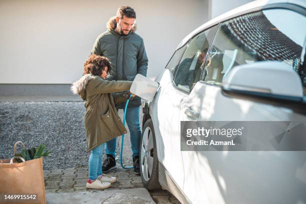 cute mixed race father and daughter charging an electric car at home - electric car home stock pictures, royalty-free photos & images