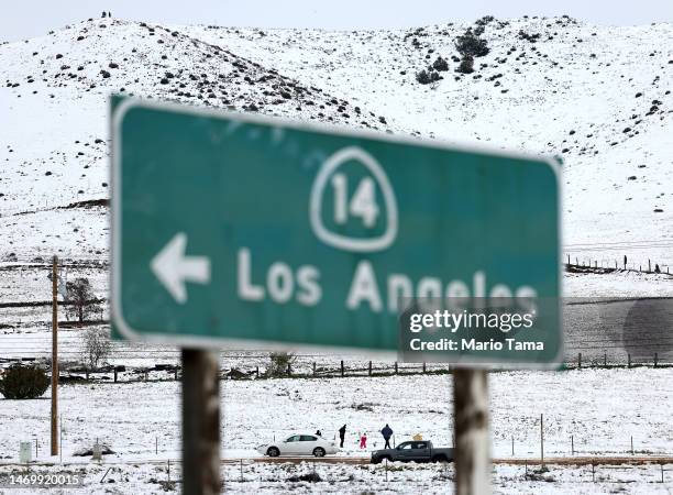 People walk in the snow near a freeway sign pointing to the city of Los Angeles on February 26, 2023 near Acton, California. A major storm, which...