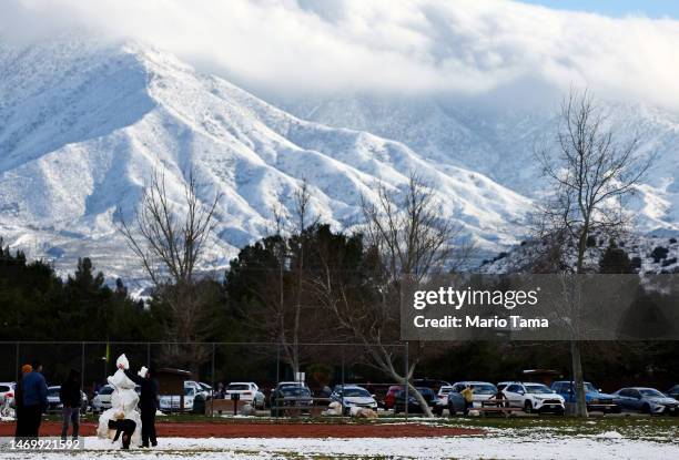 People construct a snowman in front of snow-covered mountains in Los Angeles County on February 26, 2023 in Acton, California. A major storm, which...