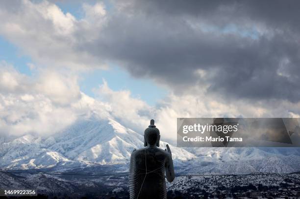 Buddha statue stands in front of snow-covered mountains in Los Angeles County on February 26, 2023 near Acton, California. A major storm, which...
