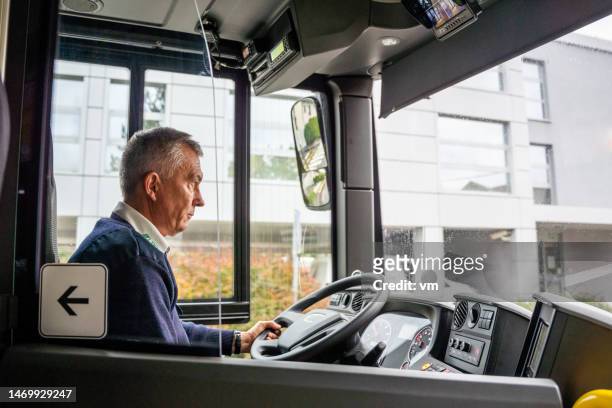senior adult male bus driver holding steering wheel - bus driver stock pictures, royalty-free photos & images