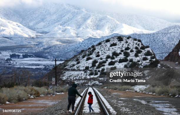 People cross railroad tracks after taking photos in front of snow-covered mountains in Los Angeles County on February 26, 2023 near Acton,...