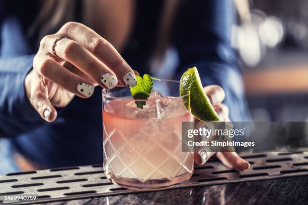 bartenders hands prepare margarita cocktail on the bar counter, she decorates the drink with a mint leaf. - garniture photos et images de collection
