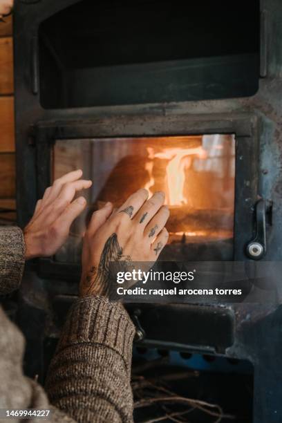 detail of an adult man's hands warming himself by the fireplace - buening shack stock pictures, royalty-free photos & images