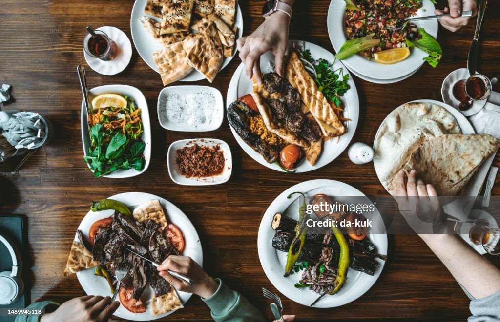 Draufsicht auf traditionelle türkische Grillgerichte mit Snacks und Gemüse auf dem Tisch. Menschen, die verschiedene Lebensmittel zu sich nehmen