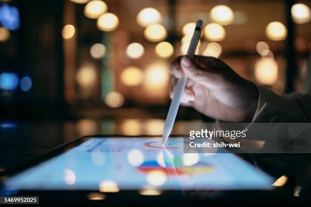 un uomo d'affari lavora in un bar di notte, utilizzando un dispositivo tablet e uno stilo per cercare gli indici dei grafici e utilizzarli per progetti di lavoro. - financials foto e immagini stock