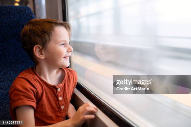 ragazzo felice che viaggia in treno durante le vacanze estive e guardando attraverso la finestra della ferrovia - bambino treno foto e immagini stock