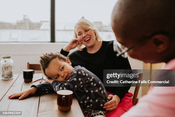 a toddler is bored as he sits between his parents at a dining table. he apathetically rests his head on his arms. - tea stock pictures, royalty-free photos & images