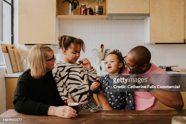 a mixed race family sit in a stylish kitchen at a table. the children enjoy snacks. - sons of anarchy stock-fotos und bilder