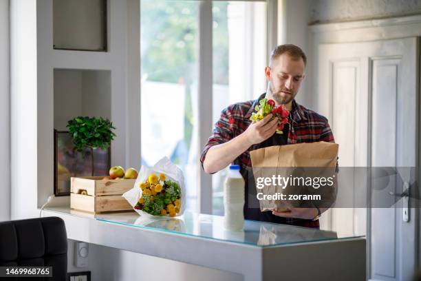 junger mann nimmt veganes essen aus papiertüte, zurück von der morgendlichen besorgung - pflanzliche ernährung stock-fotos und bilder