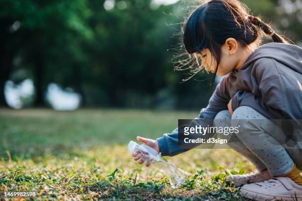 little asian girl picking up empty plastic bottle in a park and recycling. she is cleaning the environment from plastic waste. garbage recycling. sustainability and environmental protection concept - biodegradable photos et images de collection