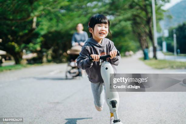 smiling little asian girl having fun riding a scooter joyfully in the park. outdoor fun. carefree and freedom concept - girl riding scooter stock pictures, royalty-free photos & images