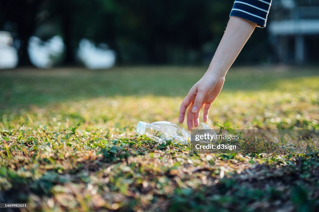 Cropped shot of a female hand picking up empty plastic bottle in a park and recycling. She is cleaning the environment from plastic waste. Garbage recycling. Sustainability and environmental protection concept