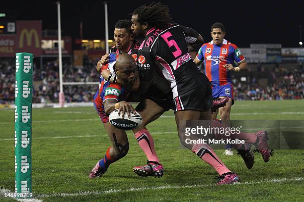 Akuila Uate of the Knights is tackled by Benji Marshall and Lote Tuqiri of the Tigers as he scores a try during the round 16 NRL match between the...