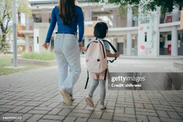a mother is holding her child's hand as they walk into the campus, sending the child off to school and preparing to embark on a brand new day of learning journey. - gedeelde mobiliteit stockfoto's en -beelden