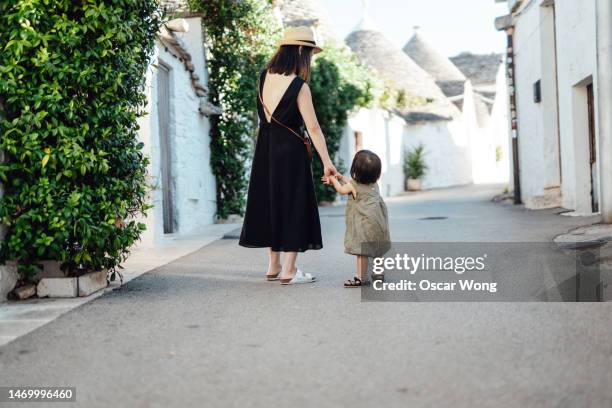 rear view of young asian mother and daughter holding hands walking in the city of alberobello, puglia, italy - alberobello foto e immagini stock