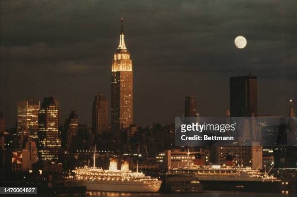 View of the Empire State Building, ships in New York harbour and skyline at night, on February 7th, 1974.