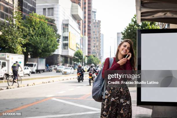 mujer joven hablando por teléfono móvil en una parada de autobús al aire libre - estudiantes universitarios bogota fotografías e imágenes de stock