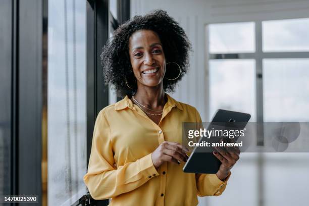 portrait of businesswoman holding tablet and looking at camera smiling - 45 year old woman stock pictures, royalty-free photos & images