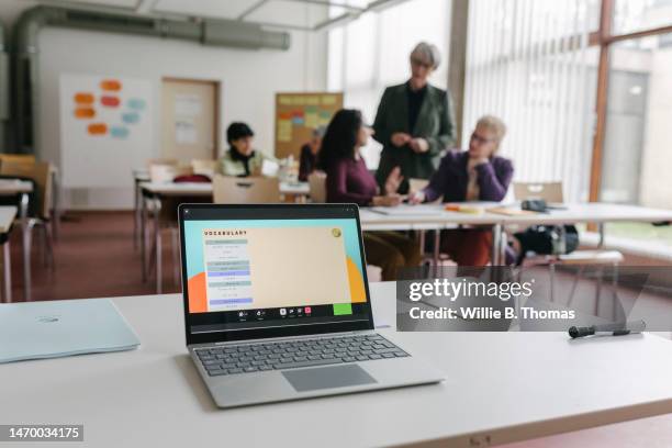 laptop on a desk while tutor talks to mature students - classroom computer stock-fotos und bilder