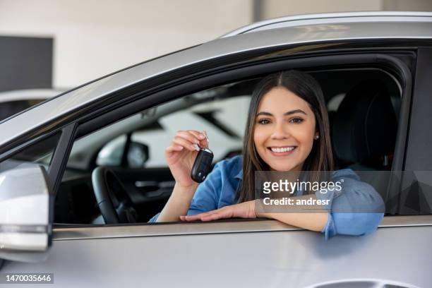 mujer feliz sosteniendo las llaves de su auto nuevo en el concesionario - auto nuevo fotografías e imágenes de stock