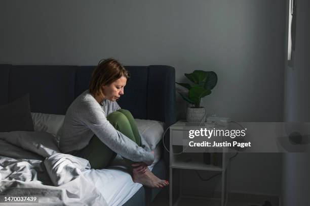powerful portrait of a mature woman sitting on her bed. she looks sad - depressione foto e immagini stock