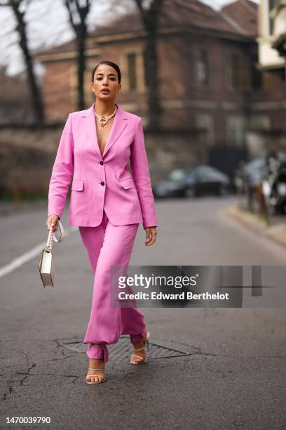 Guest wears a white pearls with large pink and red crystals pendant necklace, a pale pink buttoned blazer jacket, matching pale pink puffy suit...