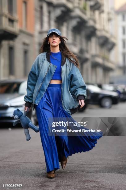 Guest wears a blue faded denim cap silver earrings, a royal blue wool cropped pullover, a blue faded denim oversized bomber coat, a royal blue...