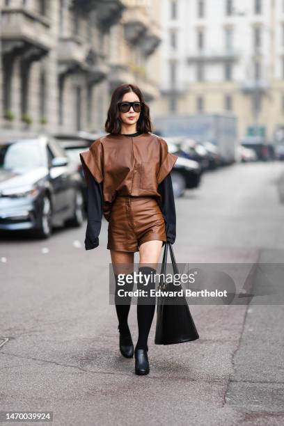 Guest wears black sunglasses, a black long sleeves t-shirt, a dark brown shiny leather oversized short sleeves t-shirt, matching dark brown shiny...