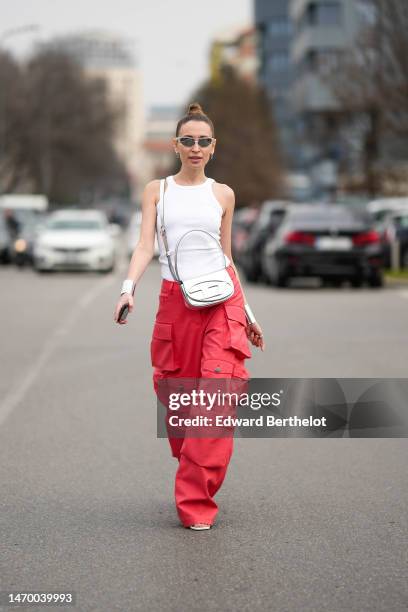 Guest wears silver sport sunglasses, a white halter neck tank-top, a silver shiny leather crossbody bag fro Diesel, red large cargo pants, white...