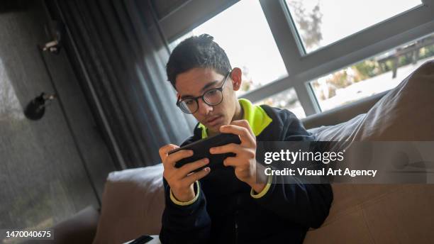 teenage boy is playing mobile game with smartphone in house focus on foreground horizontal photo - quarantine icon stock pictures, royalty-free photos & images