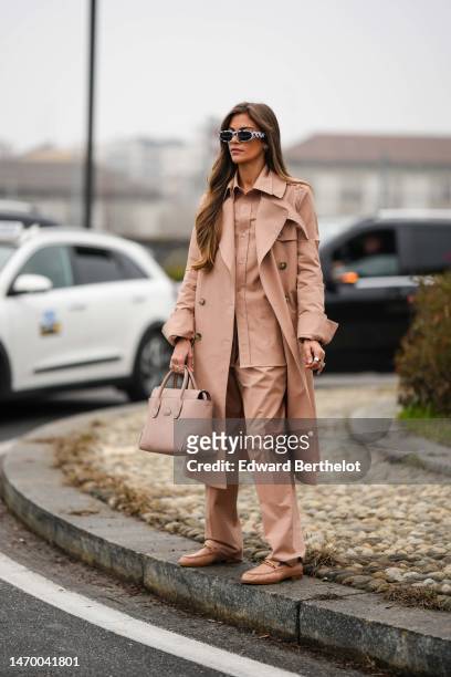 Guest wears black and white print pattern sunglasses, a beige shirt, a matching beige long coat, matching beige large suit pants, a beige matte...