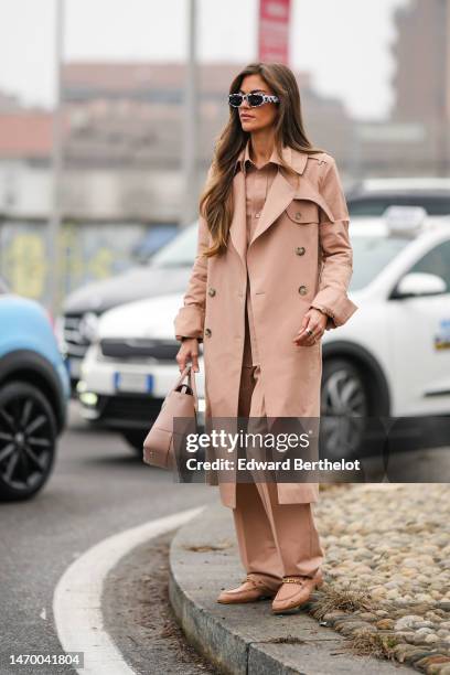 Guest wears black and white print pattern sunglasses, a beige shirt, a matching beige long coat, matching beige large suit pants, a beige matte...