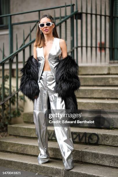 Guest wears silver hair clips, white sunglasses, silver pendant earrings, a silver shiny varnished leather V-neck / sleeveless gilet, matching silver...