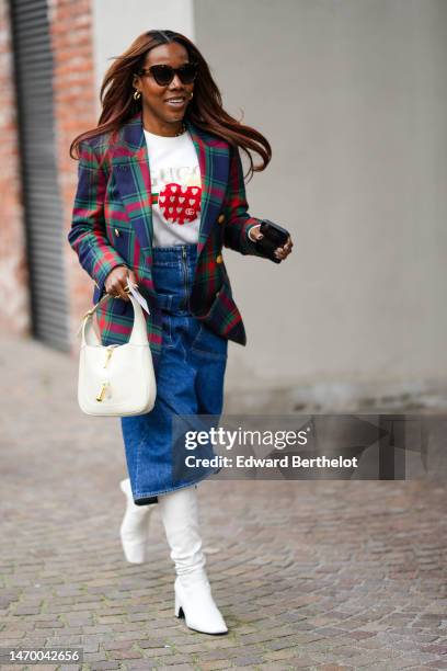 Guest wears black sunglasses from Miu Miu, gold earrings, a white with beige / red / green print pattern t-shirt from Gucci, a navy blue / green /...
