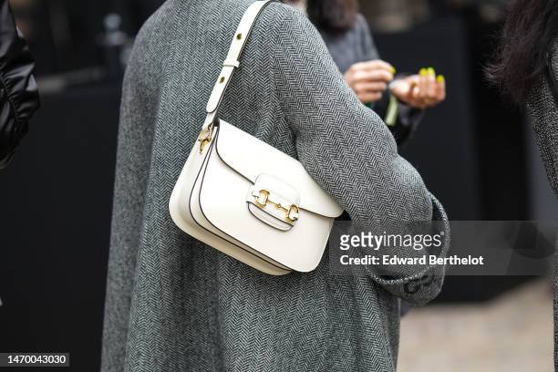 Guest wears a gray with GG monogram print pattern oversized coat from Gucci, a white matte leather shoulder bag from Gucci, outside Gucci, during the...