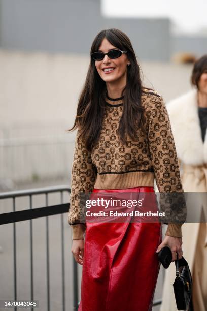 Guest wears a beige with black print pattern sweater from Gucci, a red shiny varnished leather slit / split midi skirt, a black shiny leather handbag...