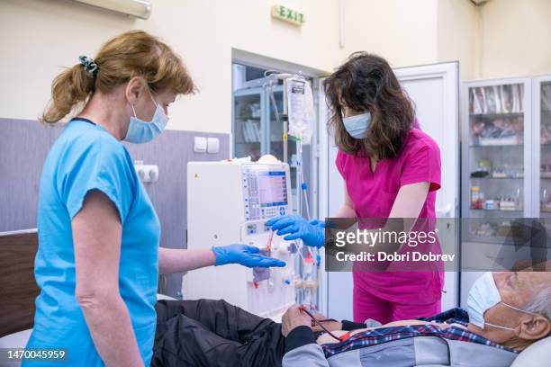 zwei krankenschwestern bereiten einen patienten auf die hämodialyse vor. - dialysis stock-fotos und bilder