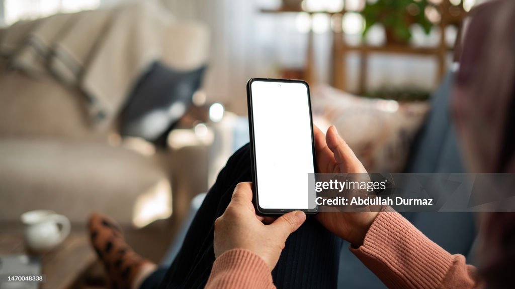 Donna che utilizza il telefono con schermo bianco mentre è sdraiata sul divano a casa, schermo di prova