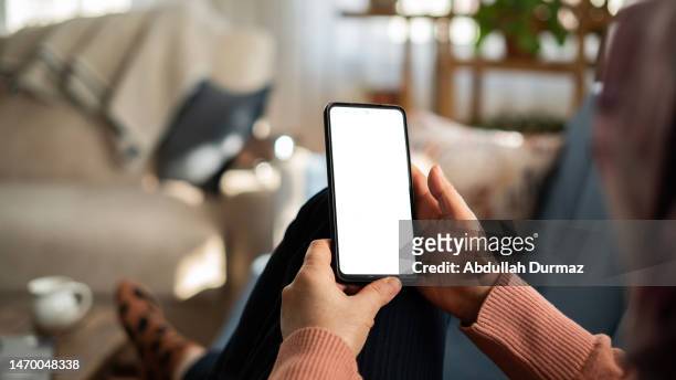 mulher que usa o telefone com tela branca enquanto está deitada no sofá em casa, tela do mock up - mão humana - fotografias e filmes do acervo