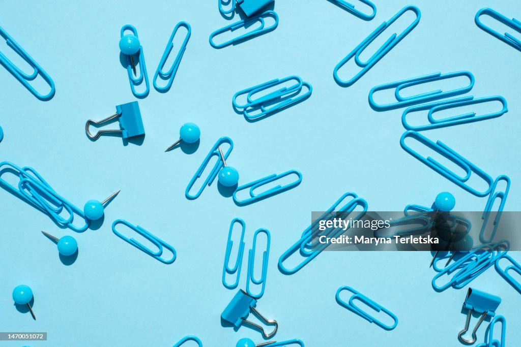 A lot of paper clips and buttons on a plain bright background. Stationery background. Back to school.