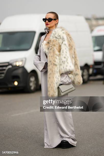 Guest wears black sunglasses from Balenciaga, silver earrings, a gray silk flower necklace, a gray silver silk blazer jacket, a pale yellow ruffled...