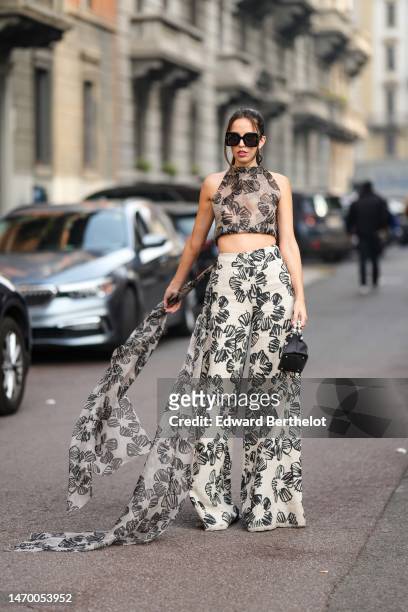Guest wears black large squared sunglasses, a beige and black print pattern tulle halter-neck / cropped top, matching beige and black print pattern...