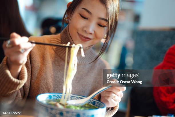 young asian woman eating beef noodle soup with chopsticks in a chinese restaurant at chinatown - japanisch chinesische küche stock-fotos und bilder