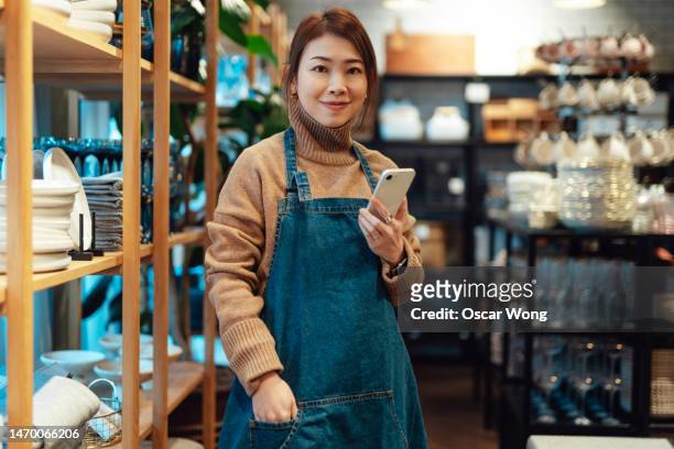 portrait of young confident business owner facing camera smiling with smartphone while at work - portrait department store stock pictures, royalty-free photos & images