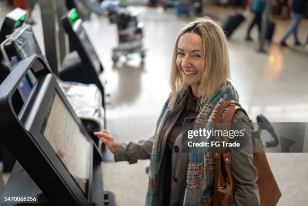 portrait of a mature woman using self service check-in machine in the airport - woman flying scarf stock pictures, royalty-free photos & images