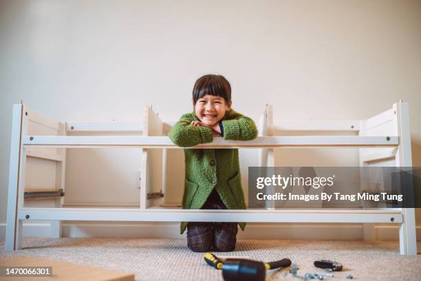 young cheerful girl smiling joyfully at the camera while playing in a half-assembled furniture - domestic room stock pictures, royalty-free photos & images