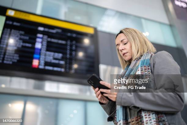 mature woman using smartphone in the airport - woman flying scarf stock pictures, royalty-free photos & images