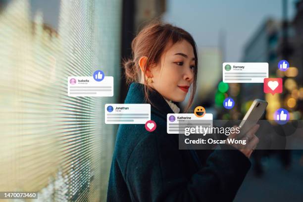 young asian business woman connecting to social media platforms with smart phone against led lights on city street - customer engagement icon fotografías e imágenes de stock
